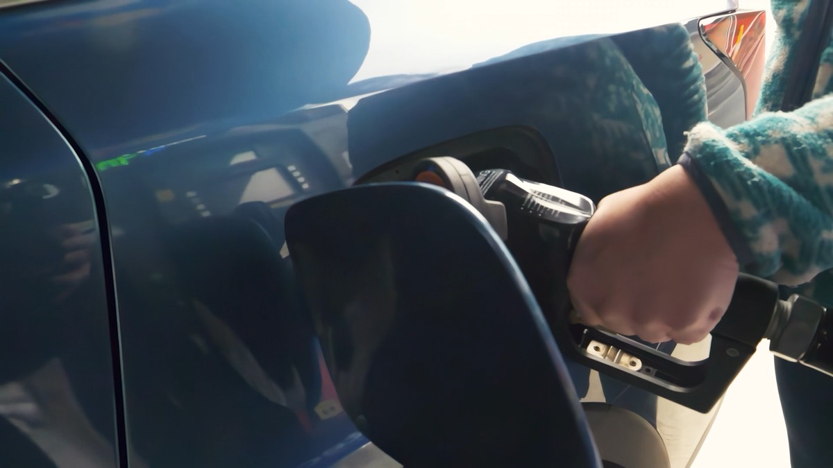 A hand holding a fuel nozzle in a car's gas tank.